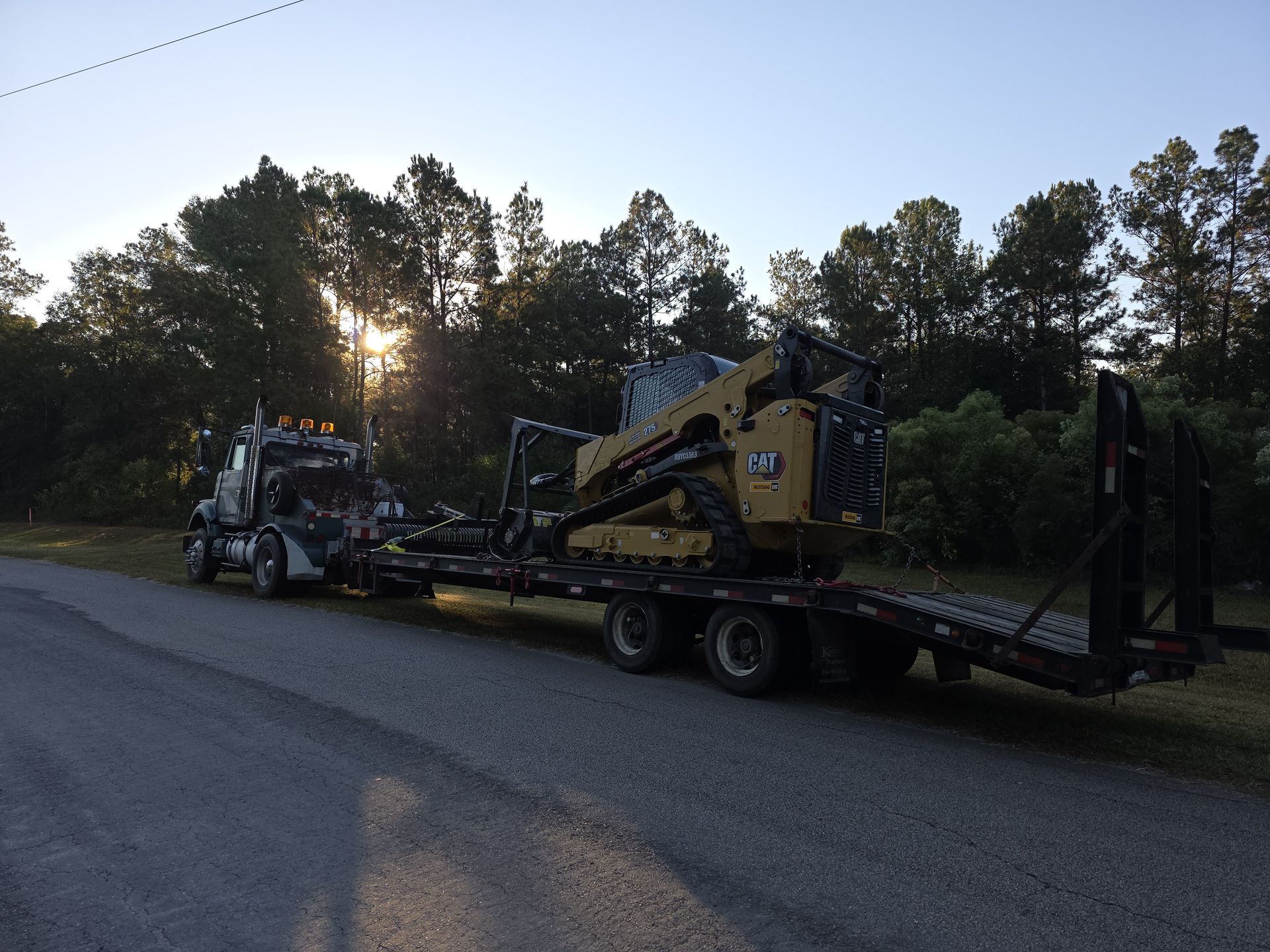 JWC Services truck hauling CAT skid steer at sunrise